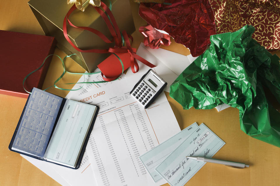 Crumpled Christmas wrapping paper and boxes on a table next to a credit card bill, cheques, a calculator and pen