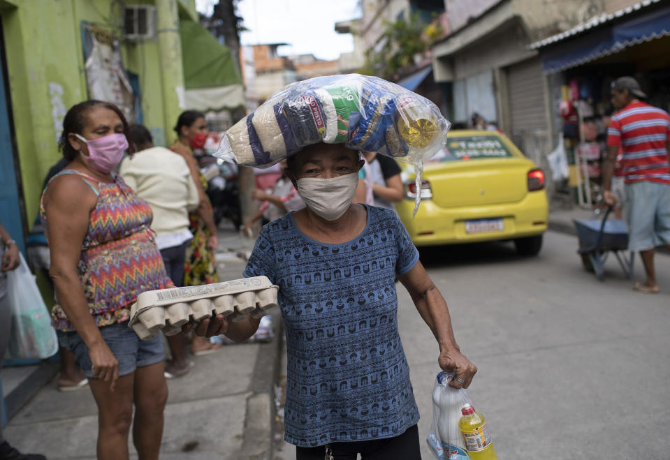 Maria Rita Dias dos Santos, wearing a protective face mask, carries to her home food donated by former inmates who are part of a nonprofit organization delivering food to people struggling due to the new coronavirus pandemic, at the Para-Pedro favela in Rio de Janeiro, Brazil, Friday, May 8, 2020. Many governments and international organizations have been stepping up amid the pandemic, providing cash transfers and food deliveries, but are facing logistical and economic hurdles. (AP Photo/Silvia Izquierdo)