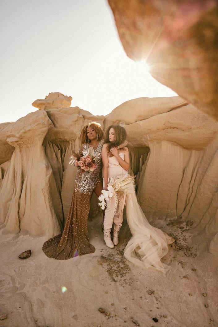 Two brides pose in front of desert rocks on their wedding day.