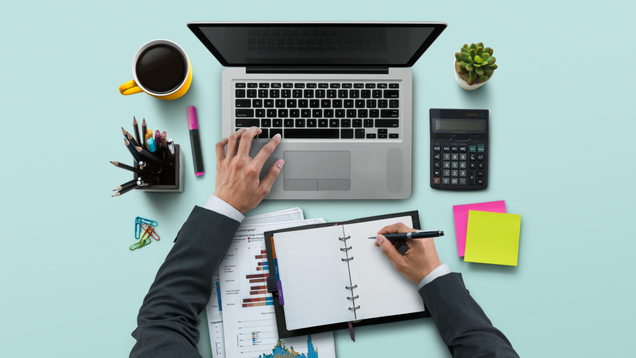 Office workplace with laptop, notebook, hand, office supplies, on turquoise background.