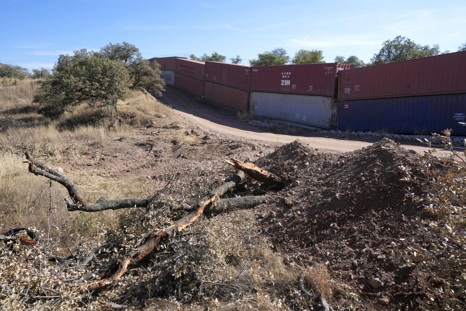 Downed trees are pushed aside on top of piles of moved dirt along the border where shipping containers create a wall between the United States and Mexico in San Rafael Valley, Ariz., Thursday, Dec. 8, 2022. Work crews are steadily erecting hundreds of double-stacked shipping containers along the rugged east end of Arizona’s boundary with Mexico as Republican Gov. Doug Ducey makes a bold show of border enforcement even as he prepares to step aside next month for Democratic Governor-elect Katie Hobbs. (AP Photo/Ross D. Franklin)