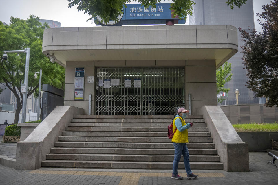 A woman wearing a face mask stands near a closed subway station in the central business district in Beijing during what is normally the morning rush hour, as most nonessential workers in the district have been ordered to work from home, Tuesday, May 10, 2022. China's capital began another round of three days of mass testing for millions of its residents Tuesday in a bid to prevent an outbreak from growing to Shanghai proportions. (AP Photo/Mark Schiefelbein)
