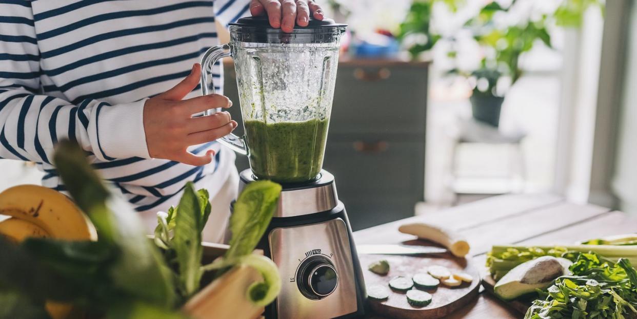 healthy eating, cooking, vegetarian food, dieting and people concept close up of young woman with blender and green vegetables making detox shake or smoothie at home