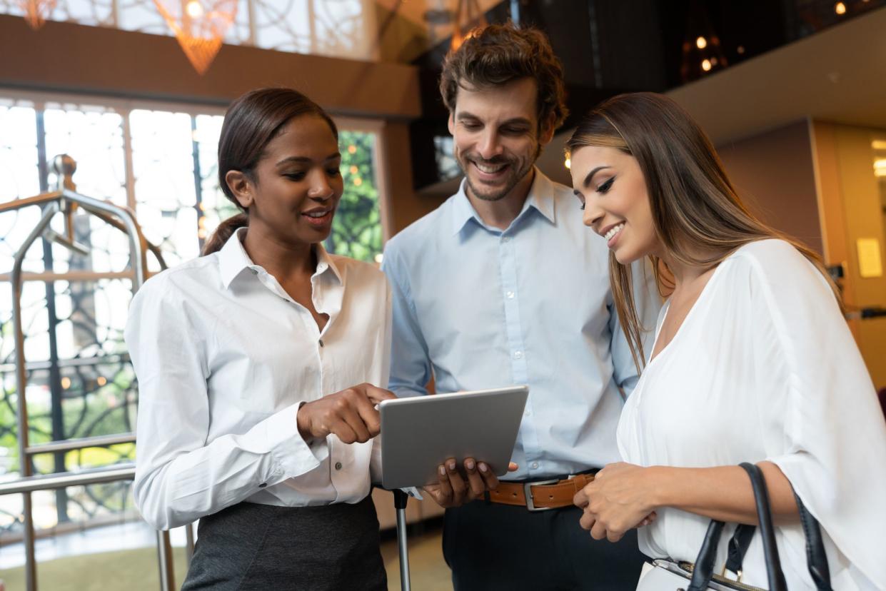 Business couple asking hotel manager for help while she shows them something on tablet all smiling