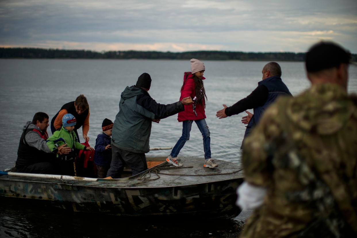 Yuri Shapovalov, center, helps people to disembark after crossing the Siverskyi-Donets river in Staryi-Saltiv, Ukraine, Wednesday, Oct. 5, 2022. Shapovalov helps locals daily to cross the river with goods as the bridge was mostly destroyed during fighting.