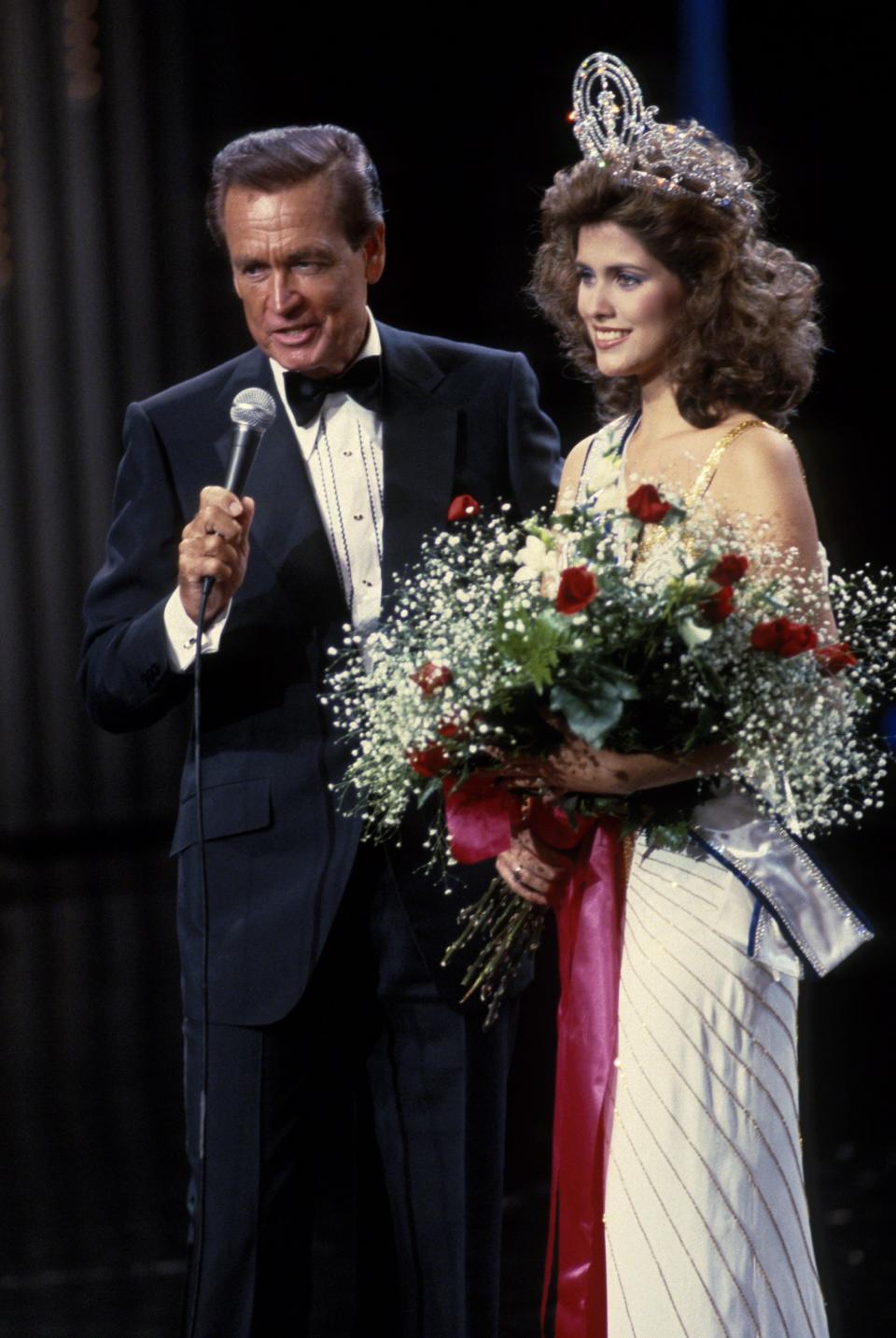 Bob Barker and Miss Universe 1985 stand on a stage.