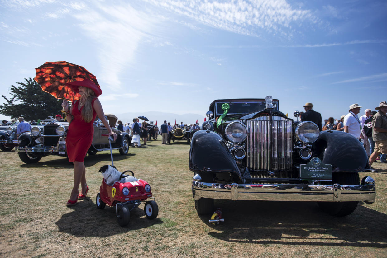 An attendee holding an umbrella and pulling a Ferrari themed cart with a dog poses for a photograph in front of a 1934 Packard 1107 Twelve Convertible Victoria, right, during the Pebble Beach Concours d’Elegance in Pebble Beach, California, U.S. At last year’s event sales of vintage cars hit a record $399 million. (David Paul Morris/Bloomberg)