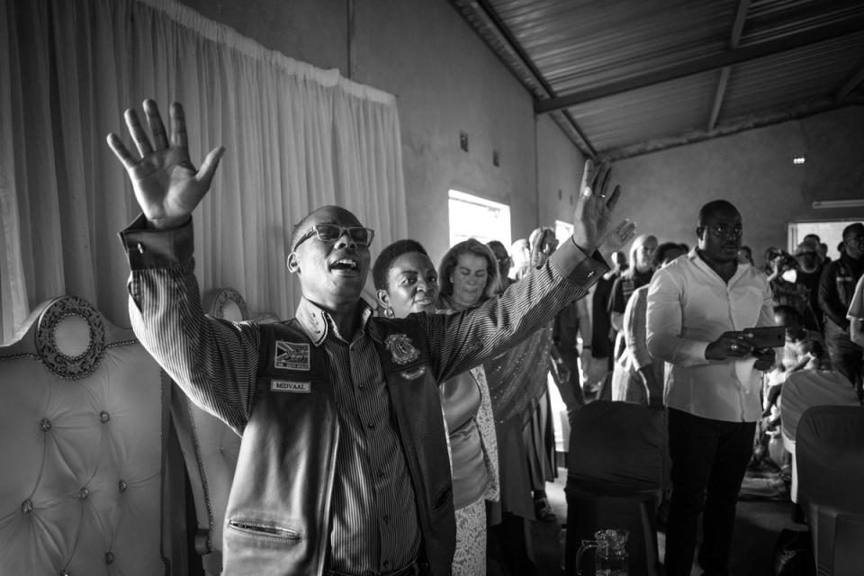 Newly patched CMA member, Pastor Doctor Danny Molapisi (left), raises his arms in prayer at his local community church in the Sebokeng township (EPA)