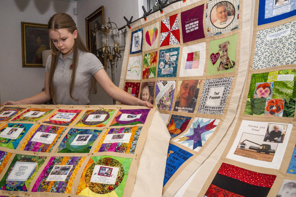 High school freshman Madeleine Fugate poses with several of her quilts, part of the COVID Memorial Quilt living memorial to honor and remember all those lost to COVID-19, at her home in Los Angeles on Wednesday, Oct. 27, 2021. Fugate's memorial quilt started out in May 2020 as a seventh grade class project. Inspired by the AIDS Memorial Quilt, which her mother worked on in the 1980s, the then-13-year-old encouraged families in her native Los Angeles to send her fabric squares representing their lost loved ones that she'd stitch together. (AP Photo/Damian Dovarganes)