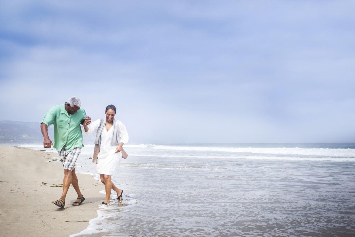 Senior African American couple walking on the beach, running from the waves