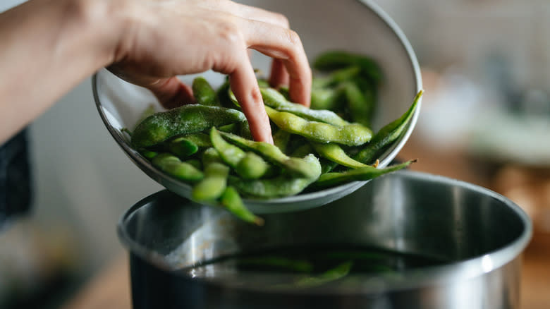person putting edamame in water