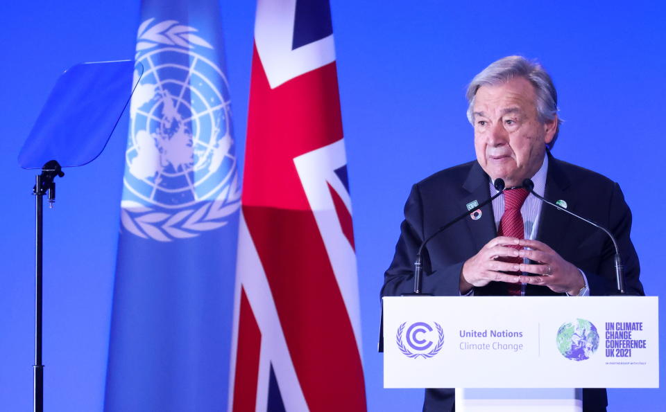 U.N. Secretary-General António Guterres speaks at a lectern, with flags of the U.N. and U.K. behind him.