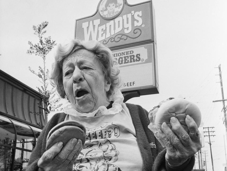 clara peller stands outside a wendy's restaurant holding two burgers