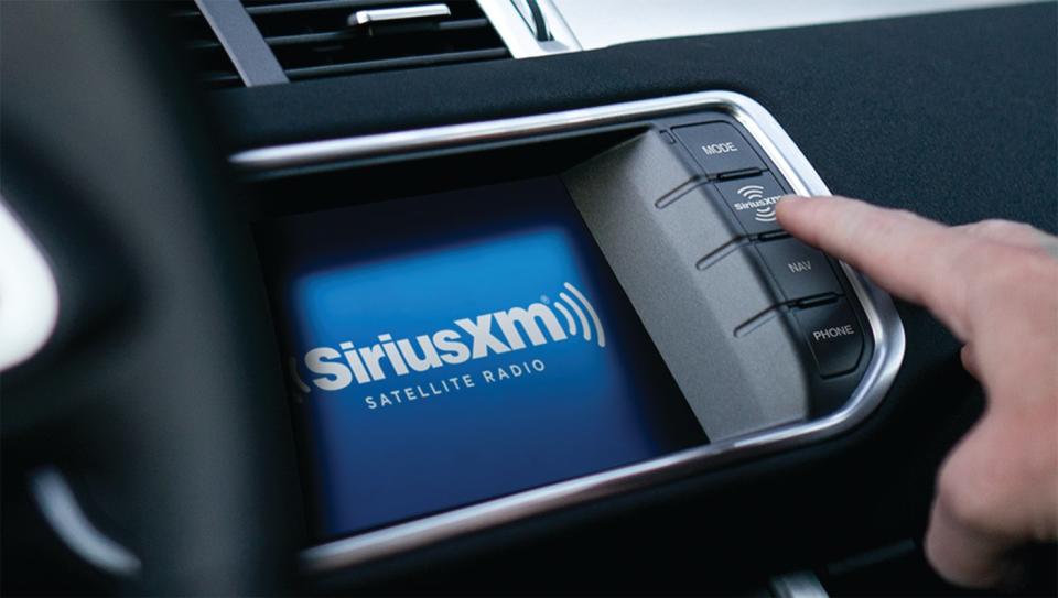 A person pressing a button on their in-car dashboard to access their Sirius XM satellite-radio service.