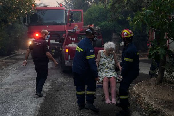 PHOTO: Firefighters evacuate an elderly woman from her house in Penteli, Greece, July 19, 2022. Hundreds of people were ordered to leave their homes after a large forest fire broke out northeast of Athens. (Thanassis Stavrakis/AP)