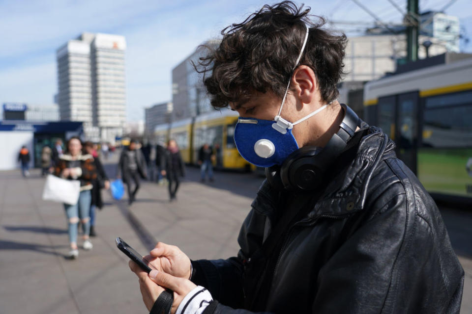 A young man visiting from Brazil and wearing a protective face mask against the coronavirus checks his smartphone while walking across Alexanderplatz in Berlin, Germany. 