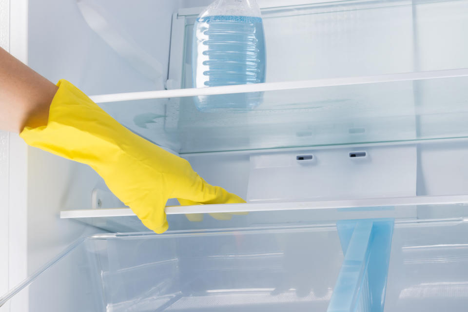 A hand in a rubber glove touching the shelves of a fridge