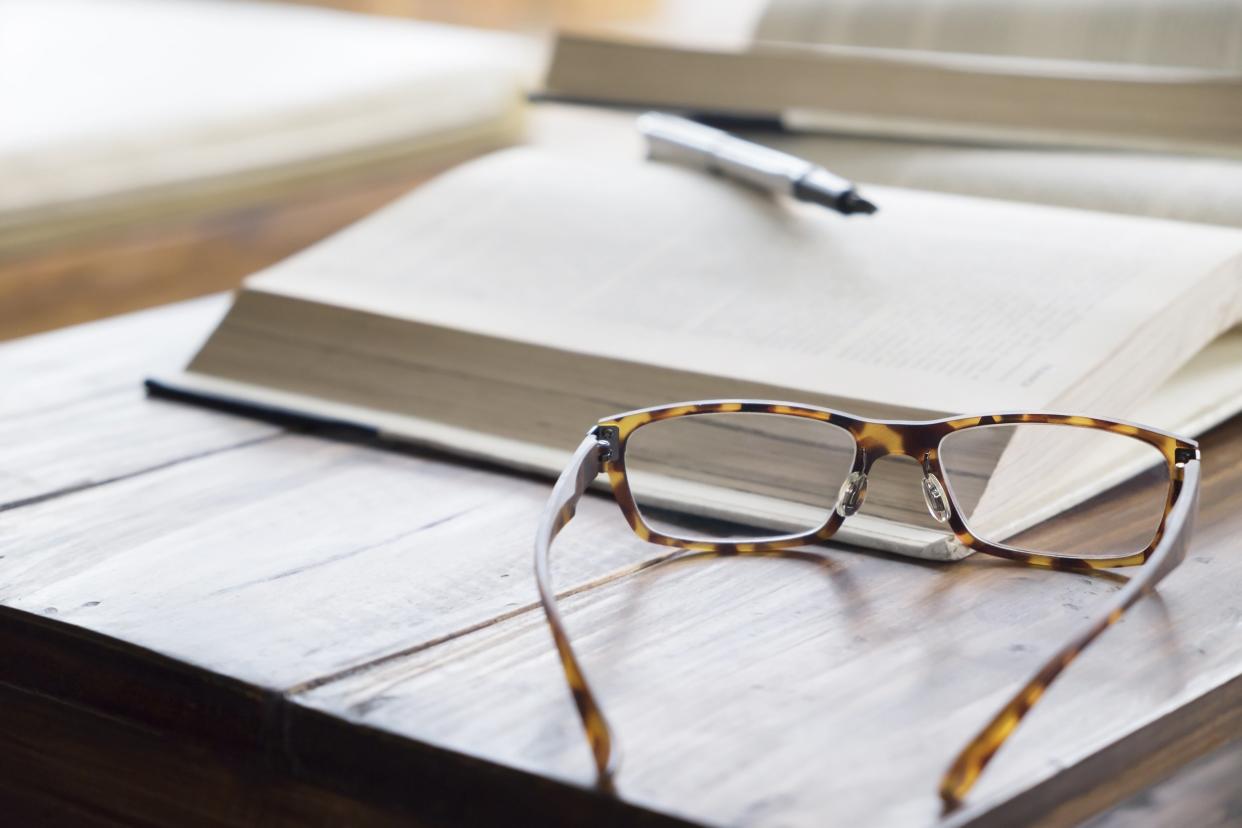 reading glasses on desk with book and pen