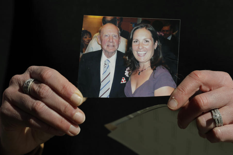 In this Wednesday, April 8, 2020, photo, Kelly Adsero holds a family photo of her grandfather Bill Chambers with her on the day she graduated as a physician's assistant in 2007. Chambers, 97, died March 14, 2020, at an adult family home where he lived with four other World War II veterans. He wasn't obviously ill, but tested positive for the new coronavirus after he died. (AP Photo/Ted S. Warren)