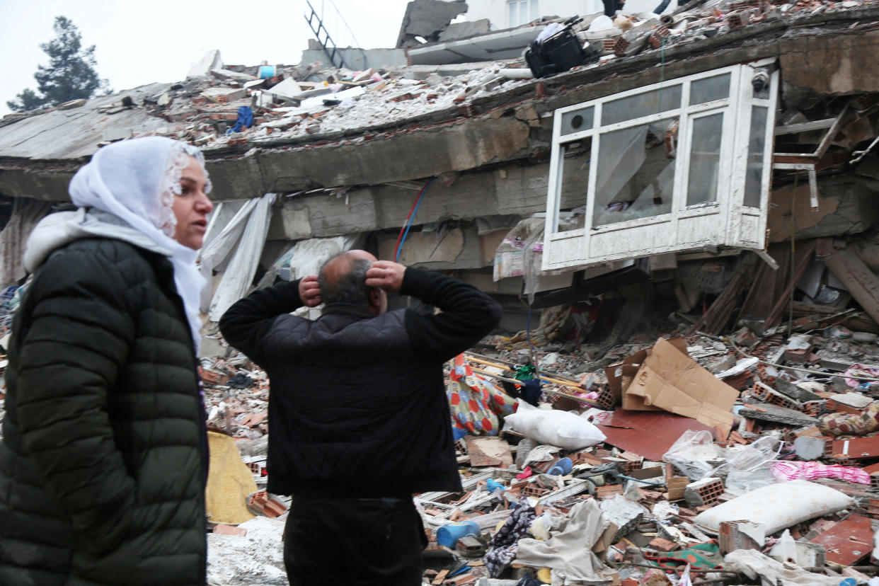 A man and a woman standing amid the rubble from a collapsed building in Diyarbakir, Turkey.