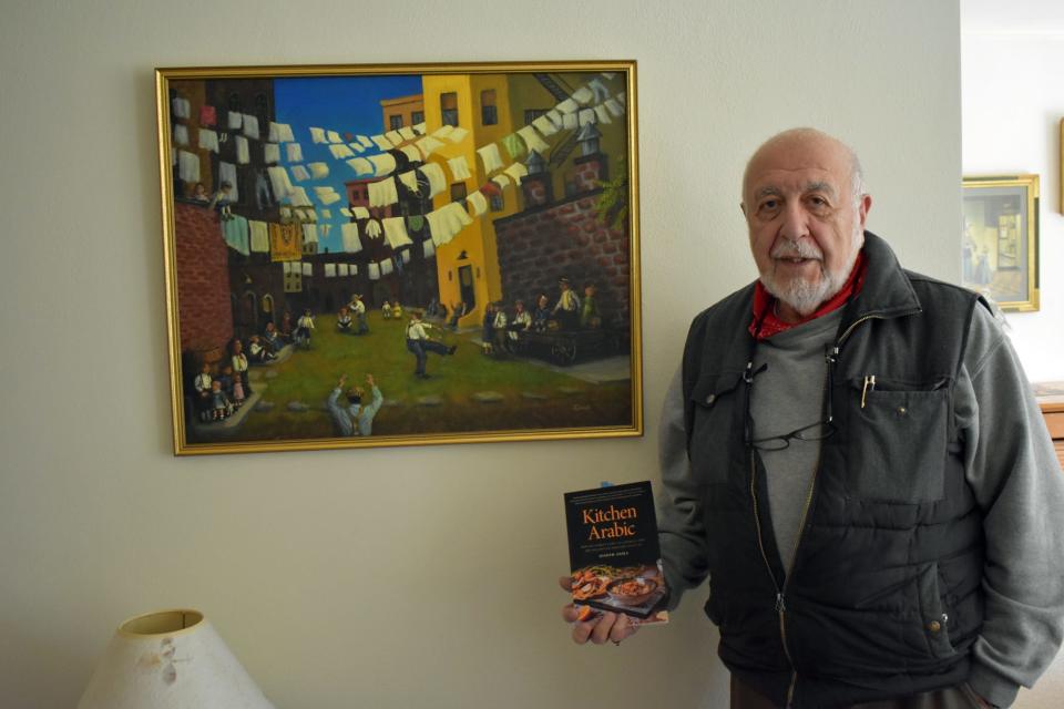 Author of "Kitchen Arabic," Joe Geha, holds his book in front of one of his paintings, "Hey Batter! Batter!"