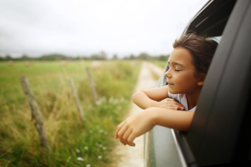 Girl with closed eyes leaning out of a car window and breathing deeply.