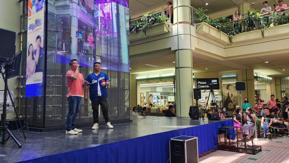 Two people stand onstage at a mall.