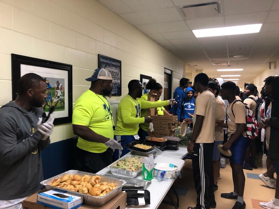 Mainland High School football coaches (left) serve food catered by BJ's Restaurant and Brewhouse to players at the school last week. Several area restaurants and businesses have reached out to support the team as it prepares to play in the state championship game on Friday. It will mark the first title-game appearance by a Volusia County school since the Buccaneers won their only championship in 2003.