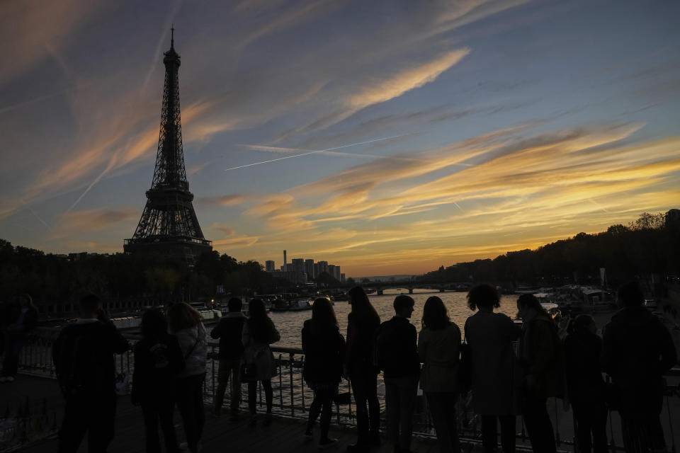 People watch the skyline as the cross the Debilly bridge near the Eiffel Tower during sunset in Paris, Saturday, Nov. 12, 2022. Paris is on track to host millions of visitors and successfully stage 32 sporting events next year when the 2024 Olympics open on July 26. That's a welcome return to business as usual for the first post-pandemic Olympics. (AP Photo/Michel Euler)