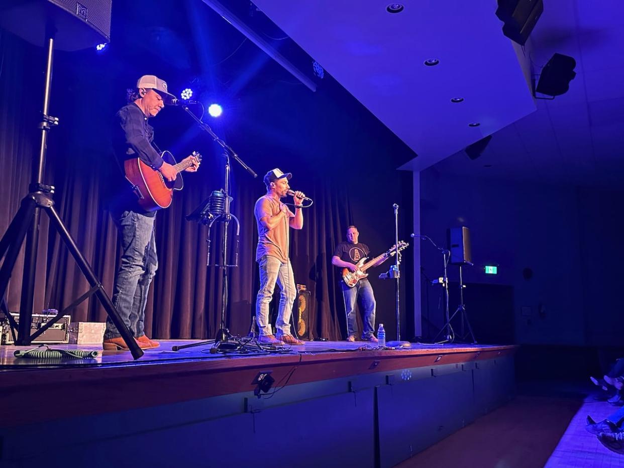 Garrett Gregory (vocals) performs with Trevor Christensen on the guitar, left, and Derrick Campbell on bass at the Bassano Community Hall in May 2024.  (Elise Stolte/CBC - image credit)