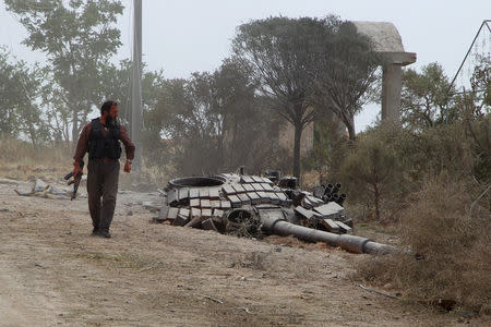 A rebel fighter carries his weapon as he walks past the turret of a damaged tank at the Mastouma military base, after they seized it, in Idlib May 20, 2015. REUTERS/Ammar Abdullah/Files