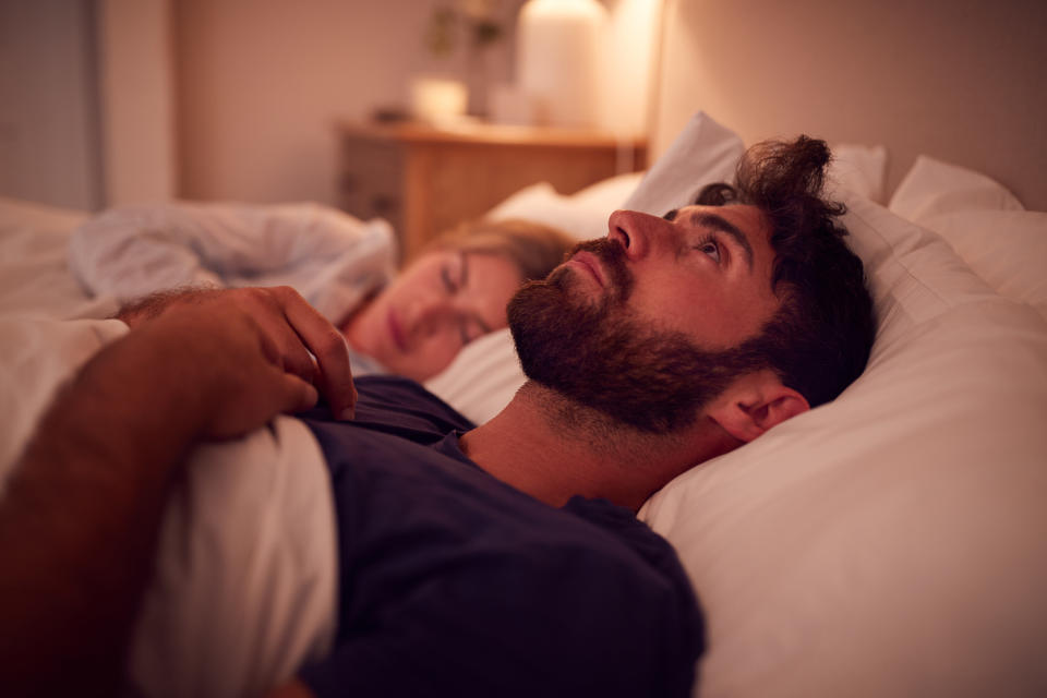 Man laying in bed awake while his partner sleeps next to him