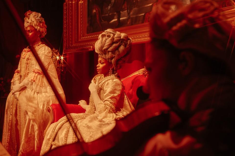 A woman with an elaborate hairdo and sits at a dress ball.