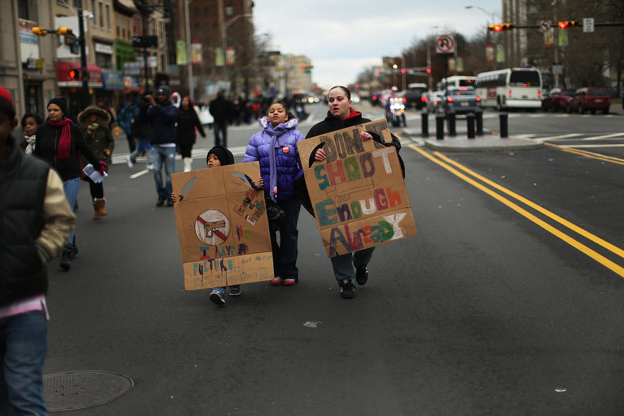 A woman marches down a main street holding a sign saying, Don't Shoot, Enough Already, with a small boy at her side holding one that says, Enough Is Enough, I Have a Future. and