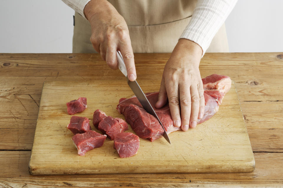 Someone cutting raw meat on a wooden cutting board