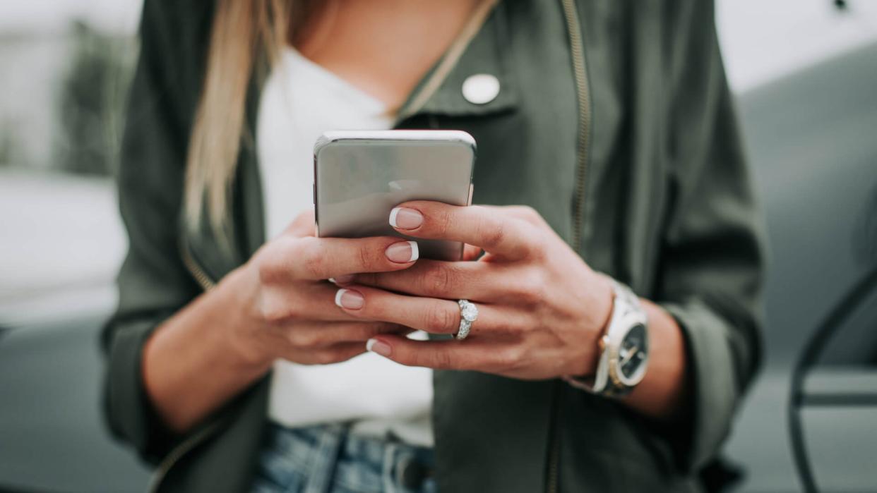 Close up female arm sending message on the phone while wearing contemporary watch and rings.