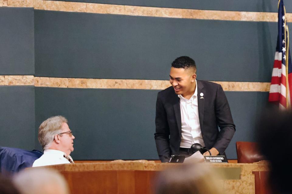 Standing and smiling, Triston Ezidore speaks with another board member during a meeting.