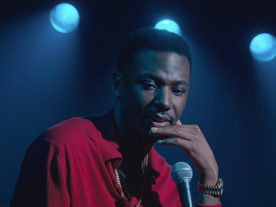 jerrod carmichael in a red shirt onstage in front of a microphone