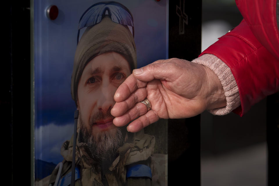 A relative touches the photograph of a fallen Ukrainian serviceman during a commemoration for the victims of the Russian occupation at a cemetery in Bucha, Ukraine, Sunday, March 31, 2024. Ukrainians mark the second anniversary of the liberation of Bucha, during which Russian occupation left hundreds of civilians dead in the streets and in mass graves in Bucha during the initial months of the Russian invasion in 2022. (AP Photo/Vadim Ghirda)