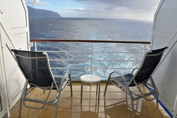 Two balcony chairs overlook the ocean behind a cruise ship after a rain shower