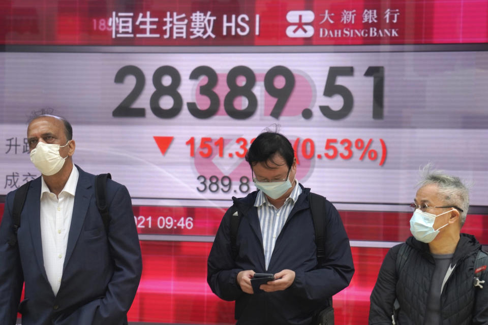 People wearing face masks to help curb the spread of the coronavirus walk in front of a bank's electronic board showing the Hong Kong share index in Hong Kong, Tuesday, March 9, 2021. Asian shares were mixed Tuesday, cheered by the imminent passage of the U.S. stimulus package, although that optimism was tempered by worries about inflation and the coronavirus pandemic. (AP Photo/Kin Cheung)