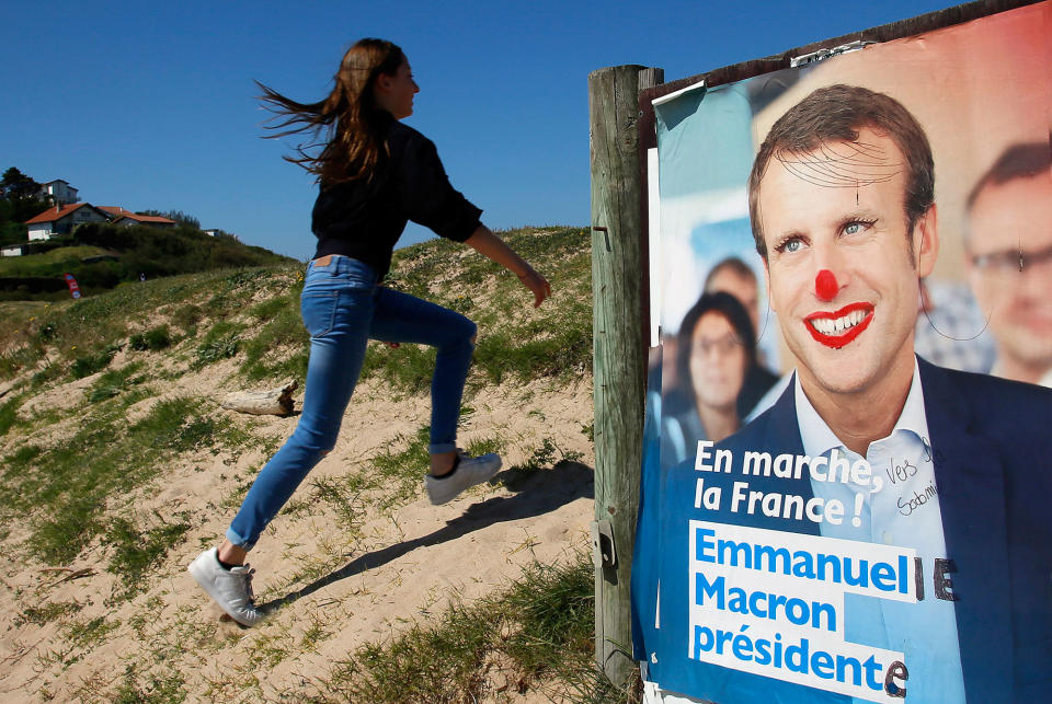 <p>A girl climbs up a dune by a defaced election campaign poster for French centrist presidential candidate Emmanuel Macron in Bidart, southwestern France, Friday, April 28, 2017. Macron will face far-right candidate Marine Le Pen in the second-round vote on May 7. (AP Photo/Bob Edme) </p>