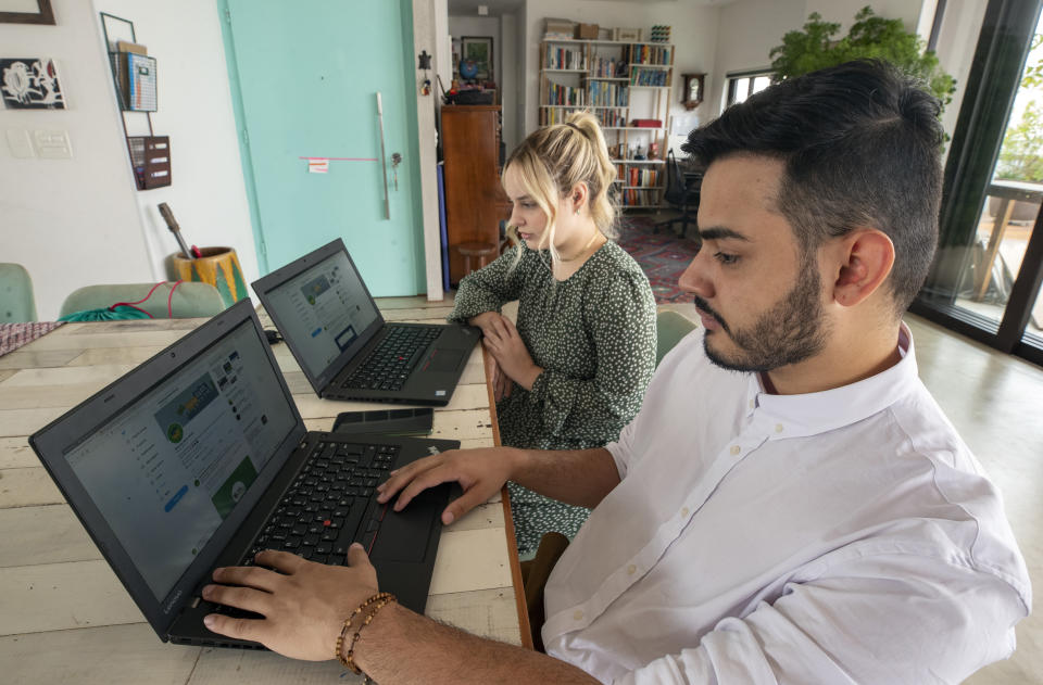 Leonardo de Carvalho Leal, right, and Mayara Stelle, who administer the Twitter account Sleeping Giants Brazil, use their computers in Sao Paulo, Brazil, Friday, Dec. 11, 2020. Sleeping Giants is a platform for activism whose stated mission is to attack the financing of hate speech and dissemination of fake news. (AP Photo/Andre Penner)
