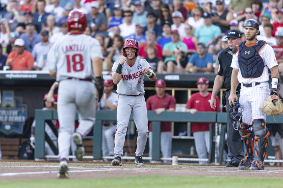 Arkansas' Michael Turner (12) scores and cheers on Chris Lanzilli (18) running home for a second run against Auburn in the third inning during an NCAA College World Series baseball game Tuesday, June 21, 2022, in Omaha, Neb. (AP Photo/John Peterson)