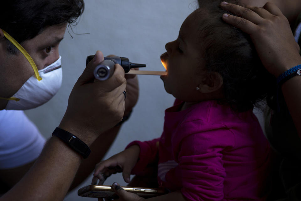 In this Oct. 26, 2019, photo, dentist Demetrio Cardenas, left, checks inside the mouth of a patient in a shelter for migrants in Tijuana, Mexico. The health crisis spans both sides of the border. In the past year, at least three children, detained by U.S. Border Patrol agents, have died from the flu while being held. They include a 16-year-old boy who was seen on security footage writhing in agony on the floor in a U.S. Border Patrol holding cell. (AP Photo/Gregory Bull)