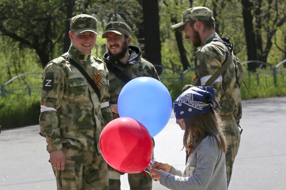 A girl holds balloons as she walks past servicemen of Donetsk People's Republic militia as they patrol a street during celebration of the 77th anniversary of the end of World War II in Mariupol, in territory under the government of the Donetsk People's Republic, eastern Ukraine, Monday, May 9, 2022. (AP Photo/Alexei Alexandrov)