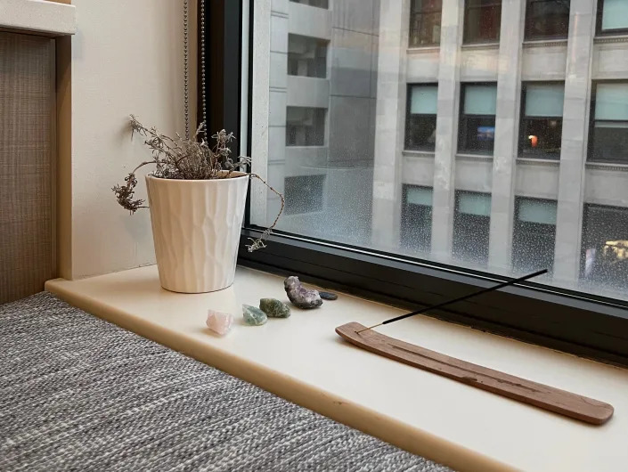 Windowsill with plant and crystals and a gray apartment building through window