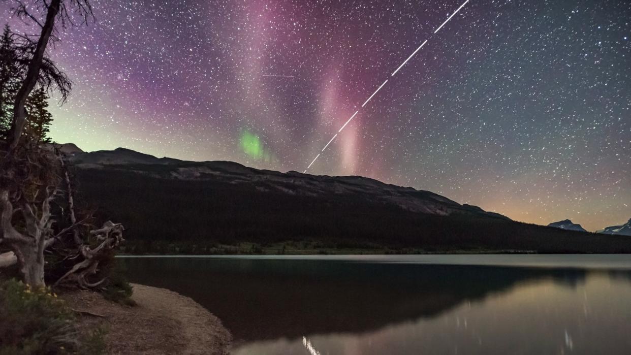  A streak of light stretches across a starry night sky above a lake. 