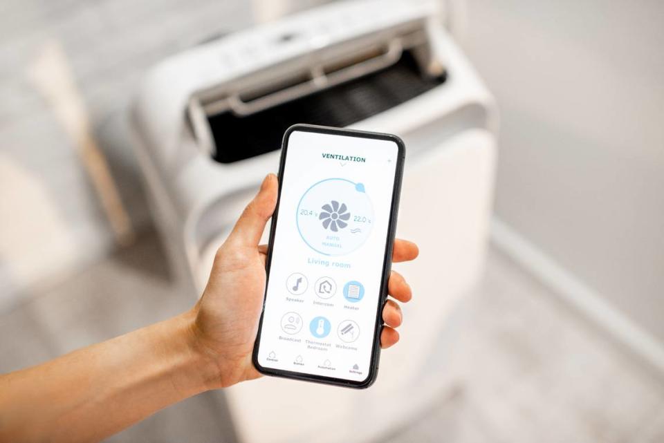 Woman holding smart phone with launched application for air condition control with ventilation unit on the background. Smart home concept