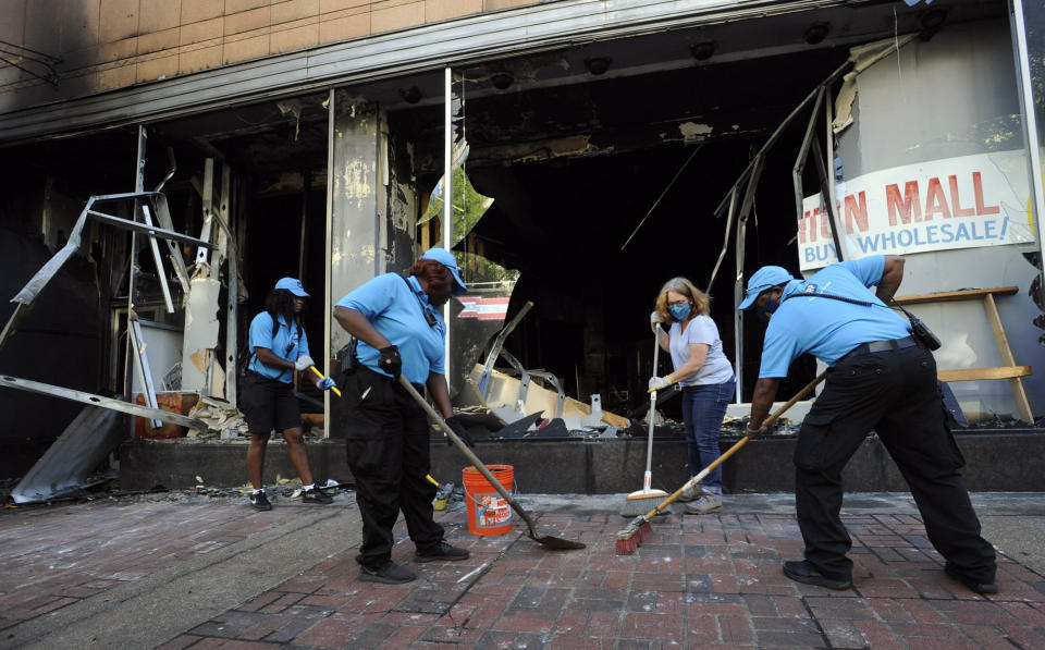 FILE - In this Monday, June 1, 2020 file photo, workers and a volunteer clean up damage outside a burned-out clothing store in Birmingham, Ala., following a night of unrest. The destruction caused by vandals and looters in cities across the country, who struck as demonstrators took to the streets in reaction to the killing of George Floyd in Minneapolis, has devastated small businesses already reeling from the coronavirus outbreak. (AP Photo/Jay Reeves)